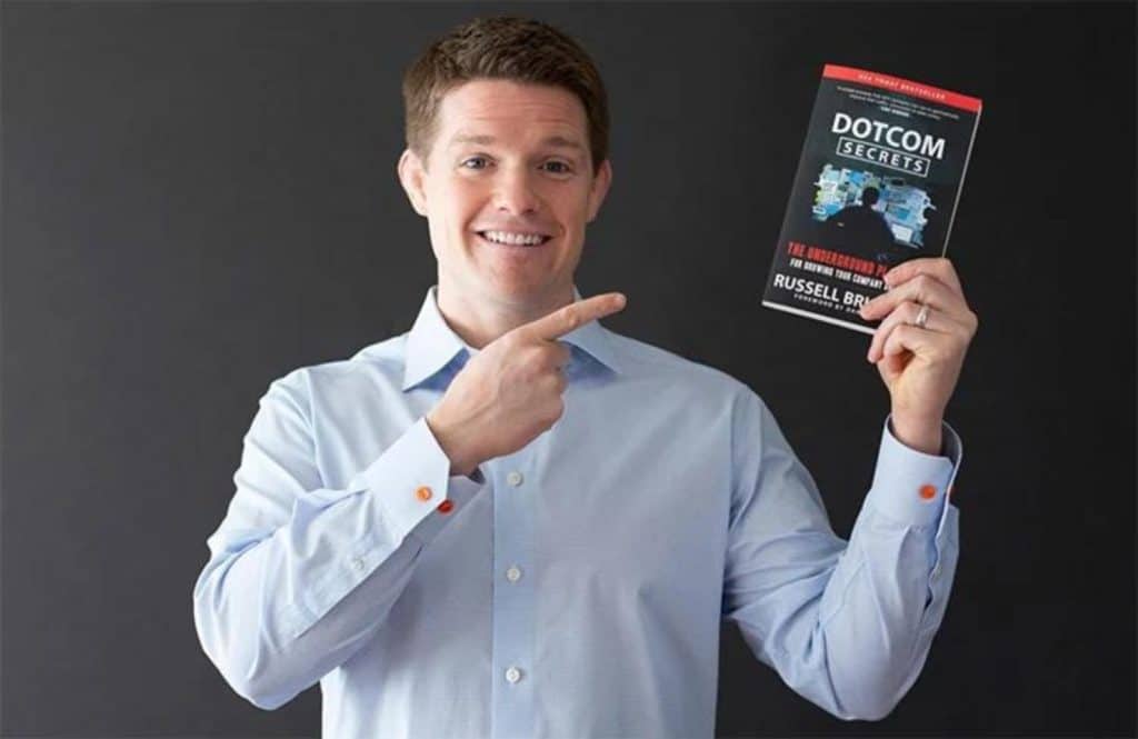 Russell Brunson is holding a copy of the book "Dotcom Secrets."